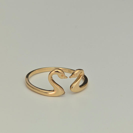 A gold open ring with a stylized swan design, resting on a white circular surface.