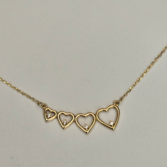 A gold chain necklace featuring three open heart pendants, each adorned with a small clear crystal, displayed against a neutral light gray background.