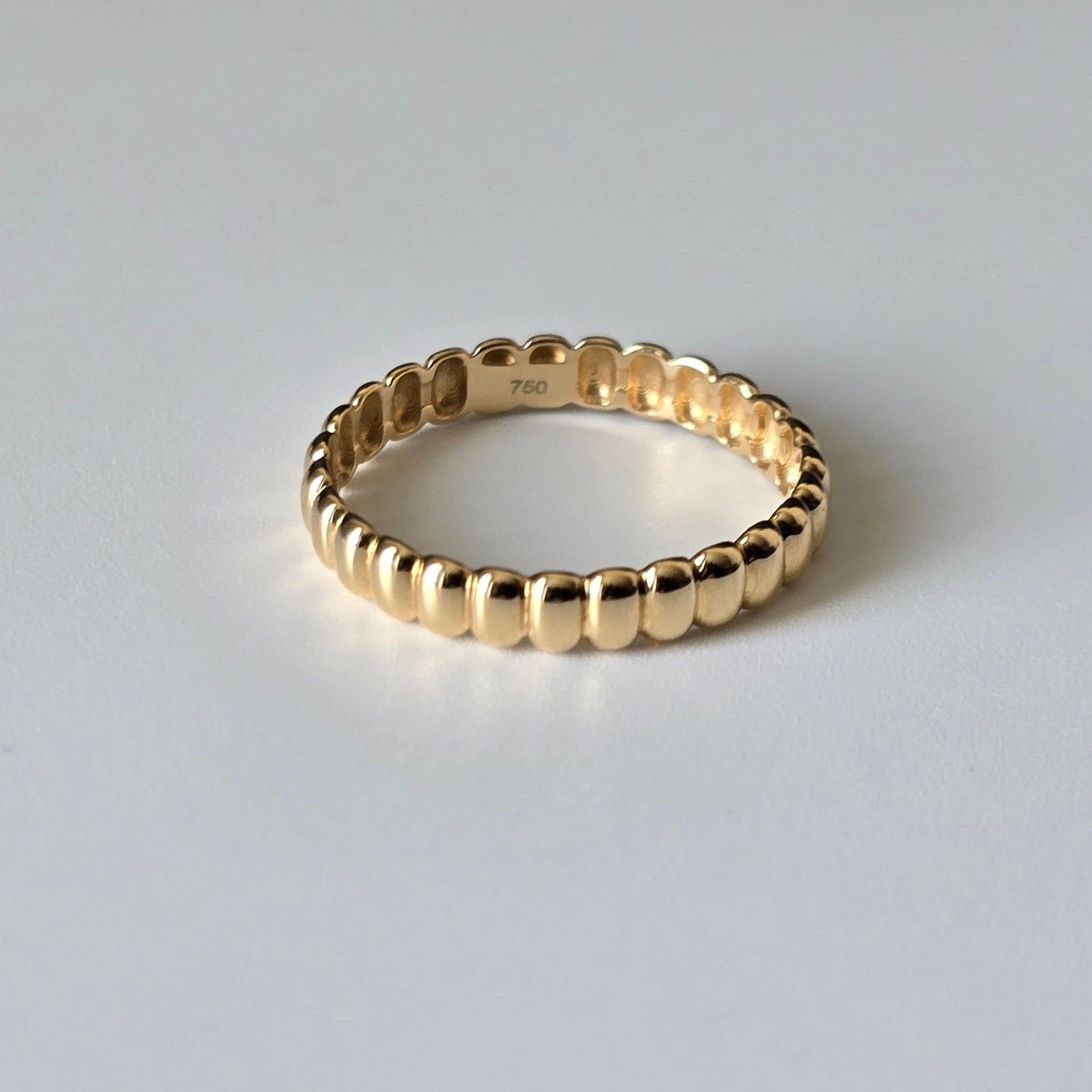 A gold beaded eternity ring with a polished finish, shown on a neutral light gray background. The inside of the band features a '750' stamp indicating 18k purity