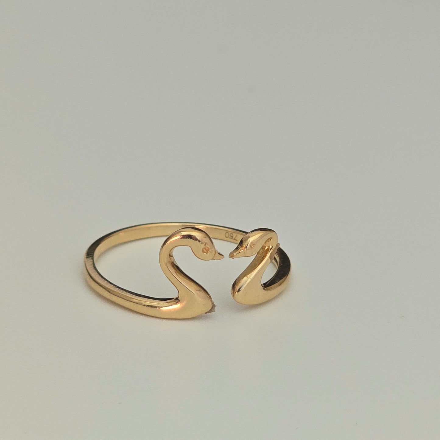 A gold open ring with a stylized swan design, resting on a white circular surface.
