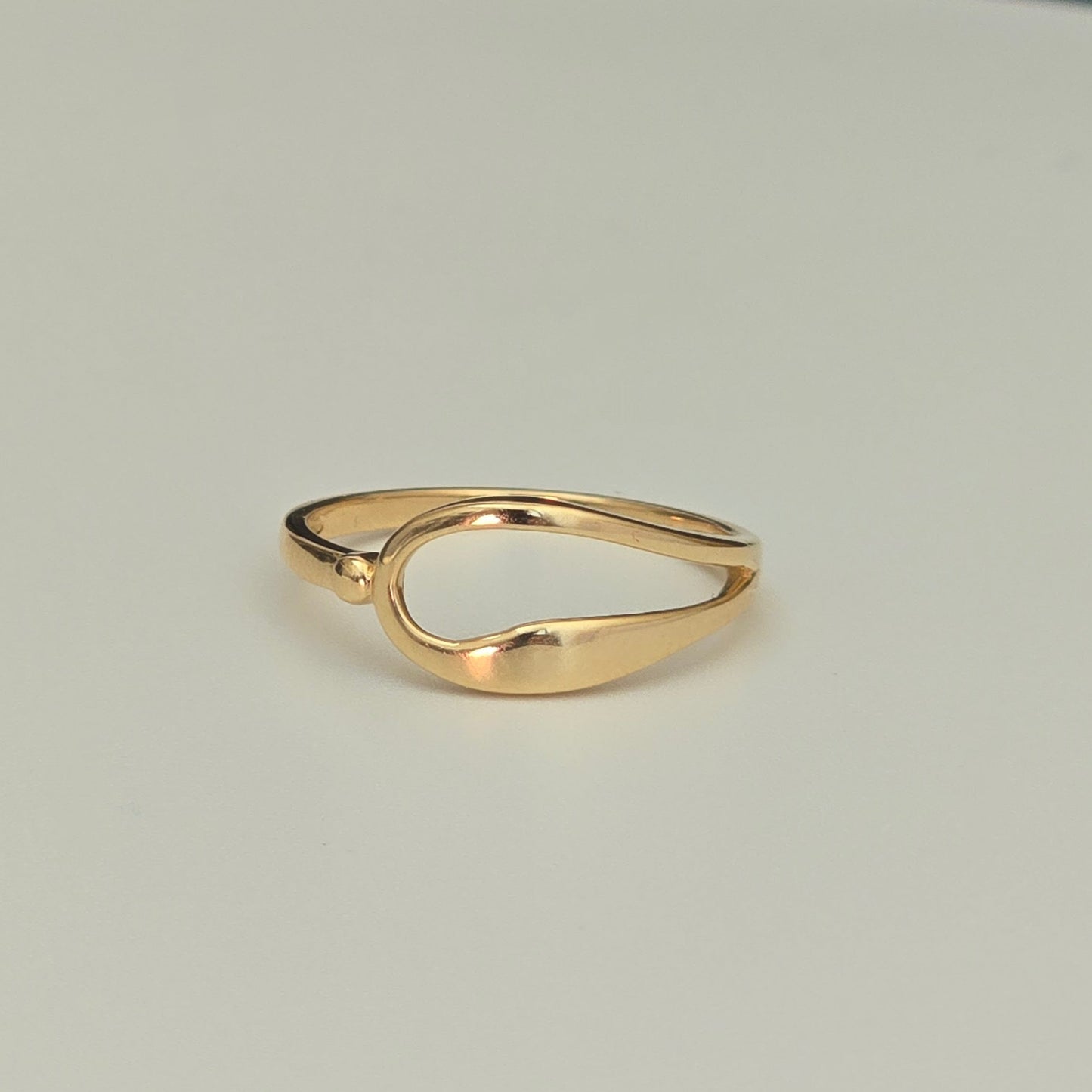 A polished gold ring with a unique, organic wavy shape, photographed on a clean, light gray background.