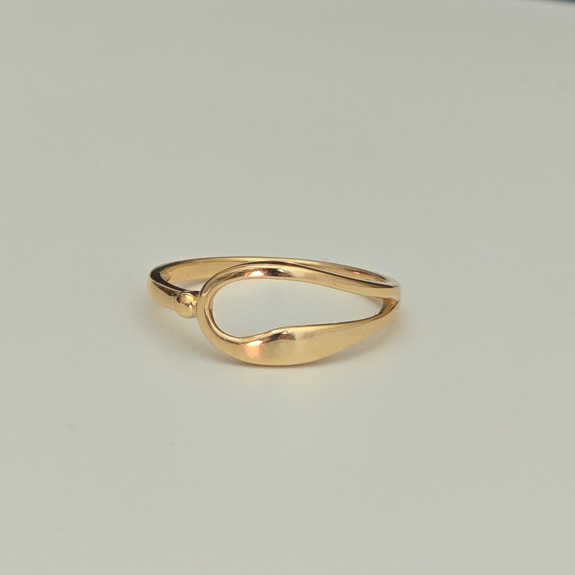 A polished gold ring with a unique, organic wavy shape, photographed on a clean, light gray background.