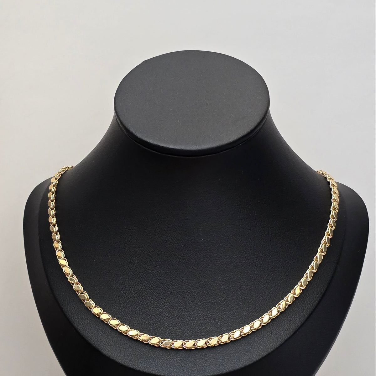 A gold-colored twisted rope chain necklace displayed on a matte black jewelry bust against a light gray background.