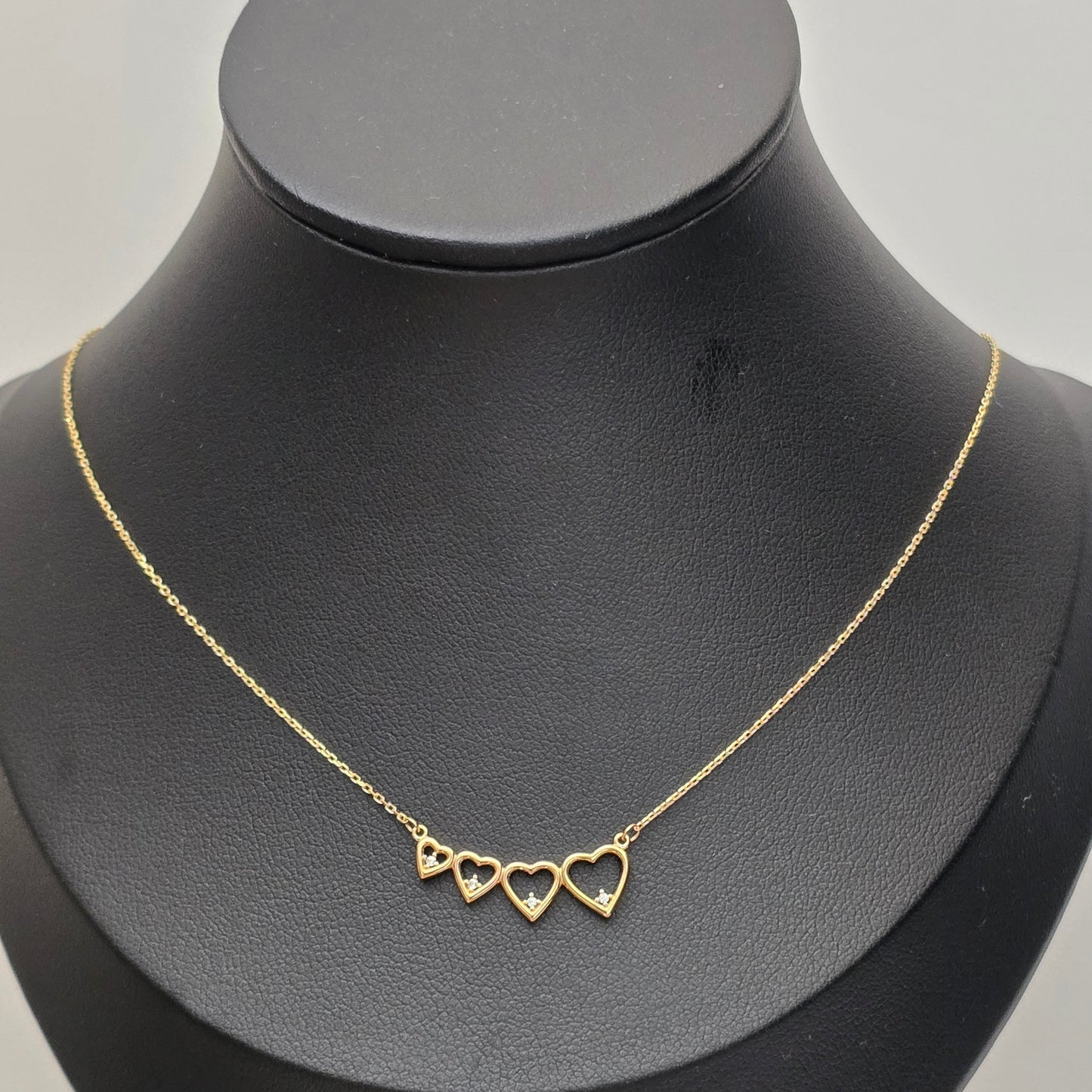 A delicate gold chain necklace with three small open heart charms, displayed on a matte black jewelry bust against a light gray background.