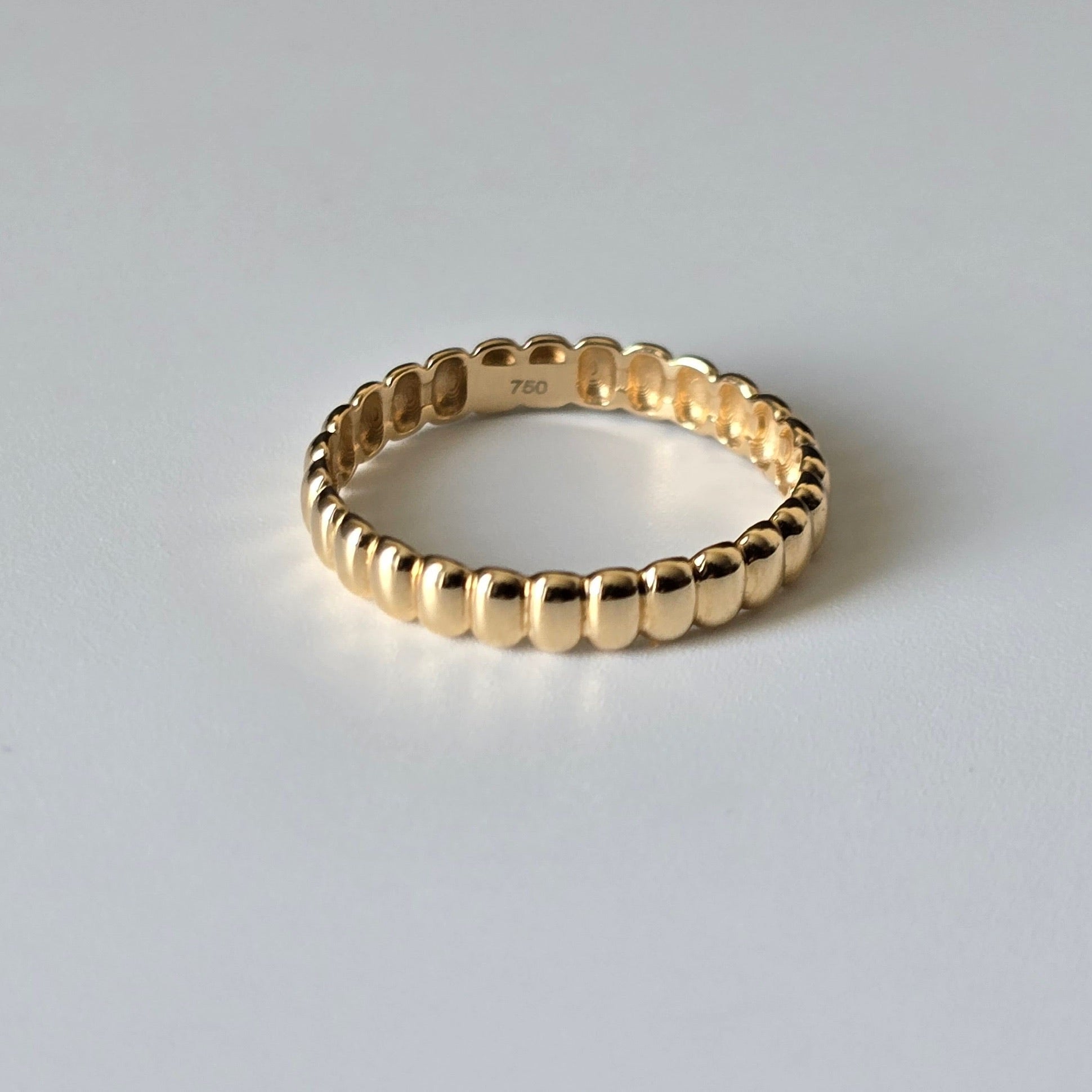 A gold beaded eternity ring with a polished finish, shown on a neutral light gray background. The inside of the band features a '750' stamp indicating 18k purity